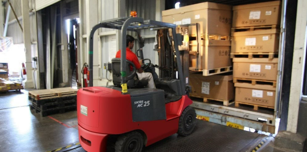 Forklift operator unloading boxes from a truck in a busy warehouse, showcasing efficient logistics operations.