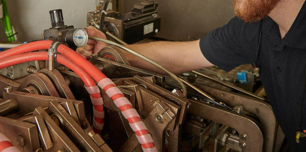 Technician adjusting machinery components and hoses in a factory setting for optimal performance and maintenance.