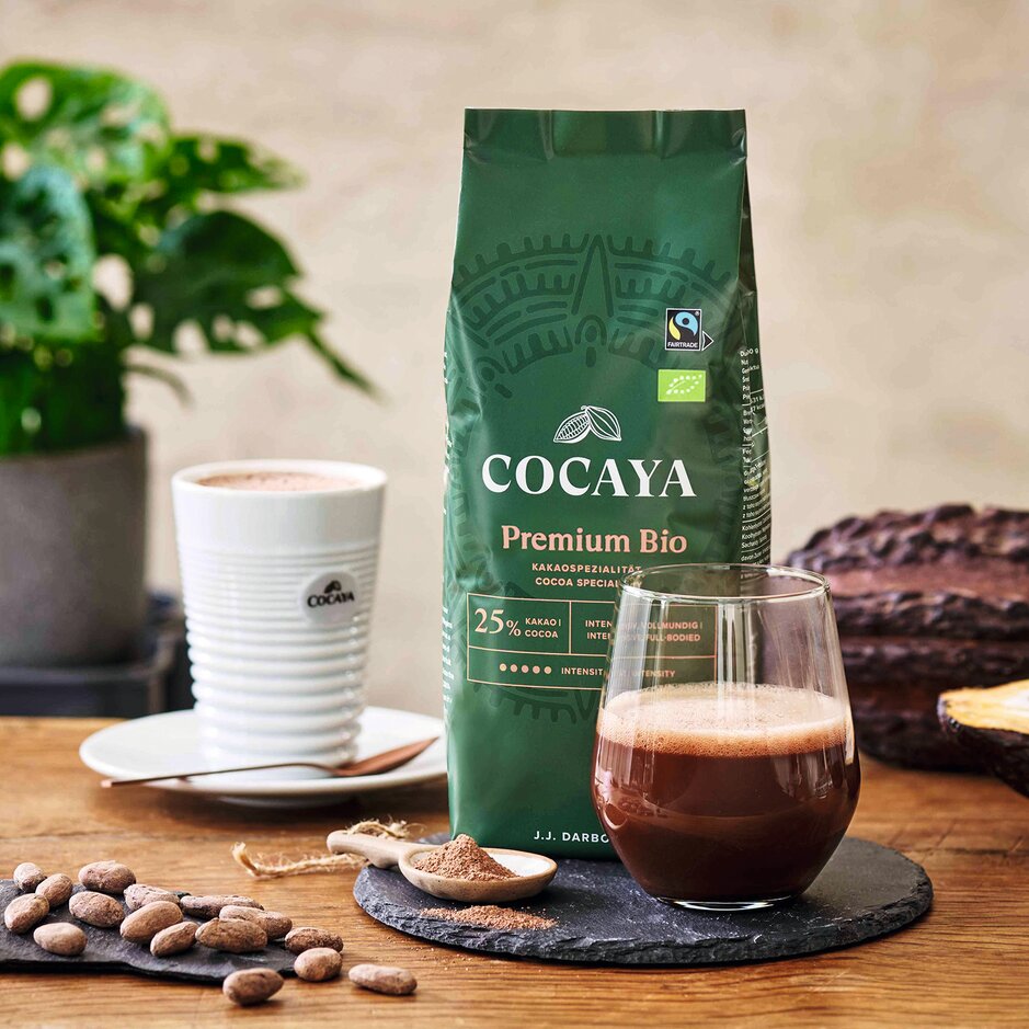 Cocaya Premium Bio-Kakao, ein frisches Getränk, Kakaobohnen und eine Pflanze auf einem Holztisch – ein Symbol für nachhaltigen Genuss.