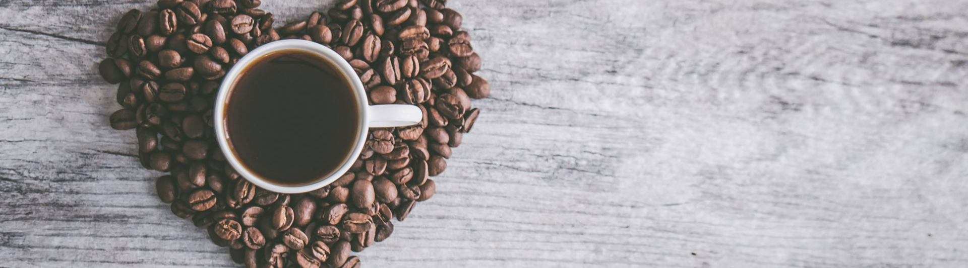 A heart-shaped arrangement of coffee beans surrounds a cup of dark coffee on a wooden table.