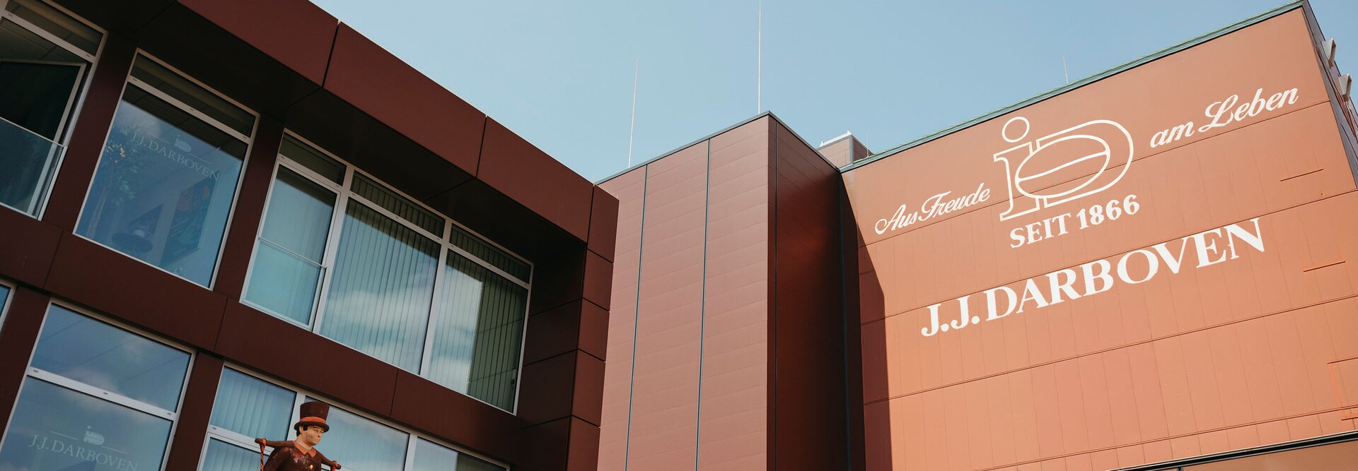 Fassade des J.J. Darboven-Gebäudes mit einer historischen Figur, die das Erbe des Unternehmens seit 1866 vor einem blauen Himmel zeigt.
