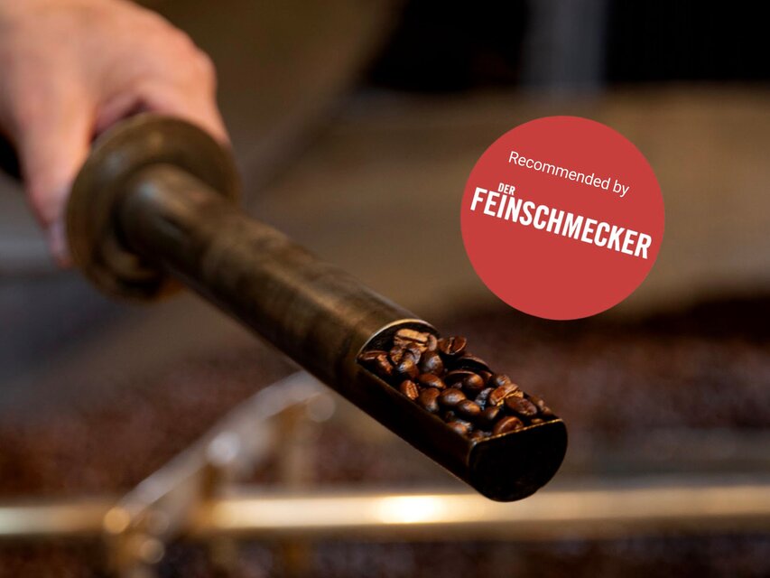 Freshly roasted coffee beans in a showcase pipe, highlighted by a "Recommended by Der Feinschmecker" badge.