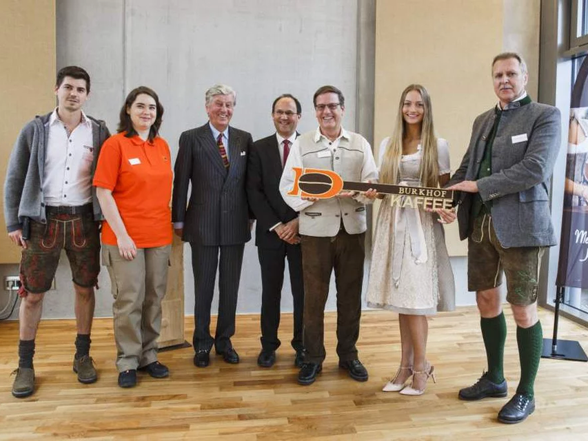 Feierlichkeiten zur Übergabe des Burkhof-Kaffees mit lokalen Persönlichkeiten in traditioneller Kleidung, die die bayerische Kultur und den Gemeinschaftsgeist hervorheben.
