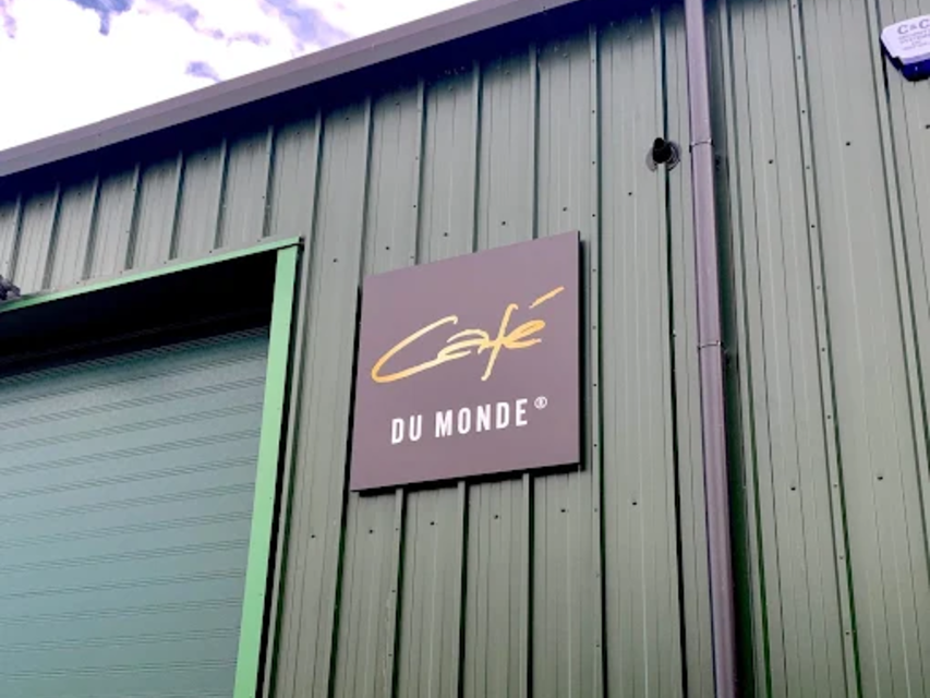 Café du Monde-Schild auf einem grünen Gebäude mit blauem Himmel im Hintergrund, bekannt für seinen Kaffee und seine Beignets in New Orleans.