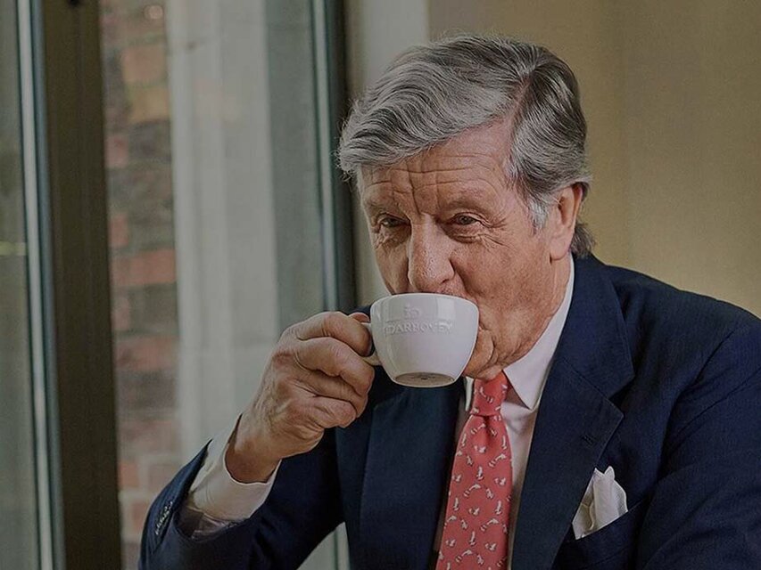 Ein kultivierter Mann genießt einen Kaffee in einem Café, umgeben von elegantem Dekor und einem Blick auf die Straße.