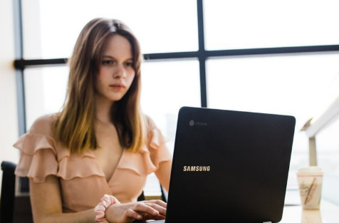 Junge Frau mit einem Samsung-Laptop in einem modernen Arbeitsbereich, konzentriert auf ihre Arbeit, mit einem Kaffee zum Mitnehmen in der Nähe.