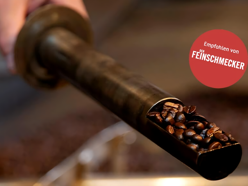 Metallschaufel gefüllt mit gerösteten Kaffeebohnen, versehen mit einem Empfehlungssiegel der Zeitschrift Feinschmecker.