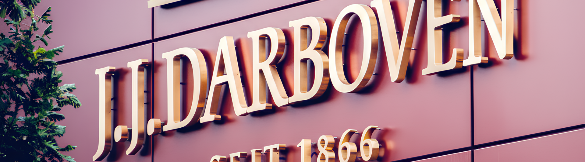 Schild des 1866 gegründeten Unternehmens J.J. Darboven mit elegantem Schriftzug auf einer modernen, begrünten Fassade.
