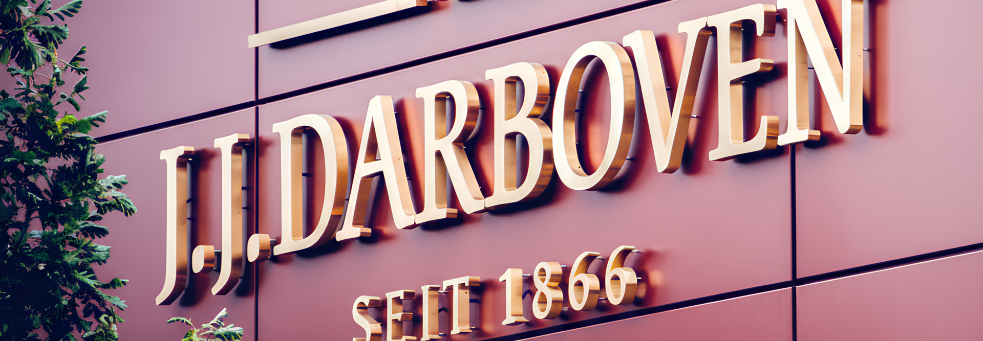 Schild des 1866 gegründeten Unternehmens J.J. Darboven mit elegantem Schriftzug auf einer modernen, begrünten Fassade.