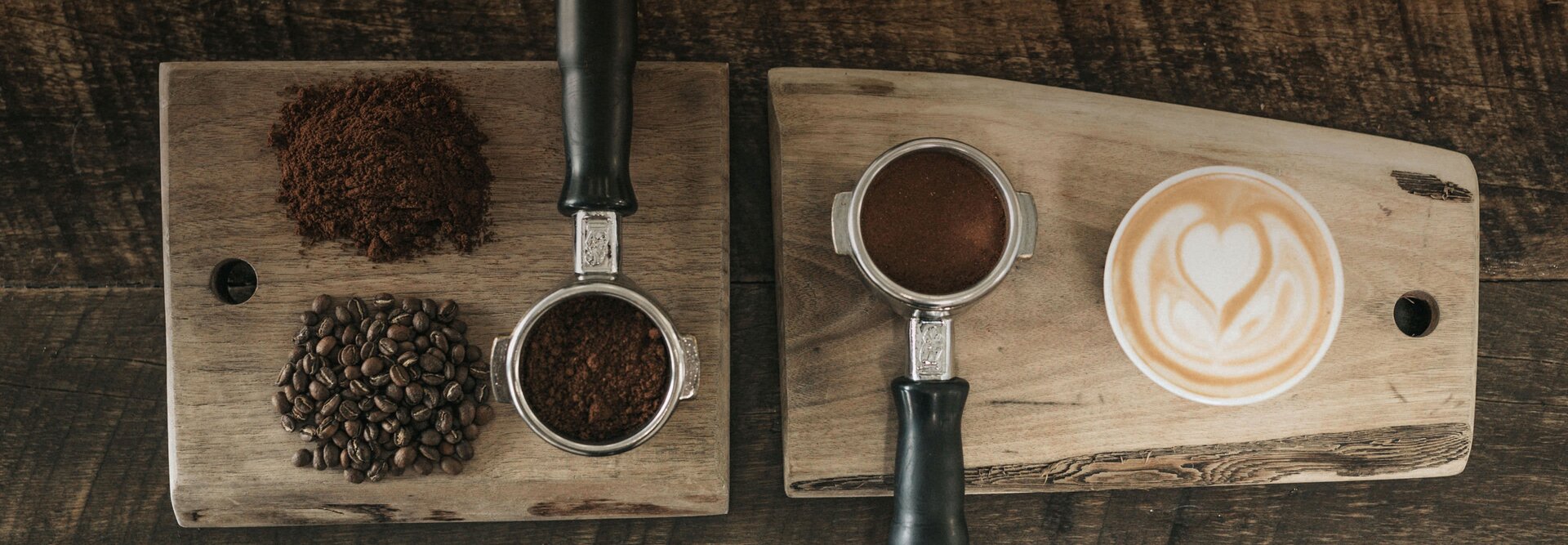 Frisch gemahlener Kaffee und Bohnen gepaart mit einer schön gestalteten Latte Art auf Holzbrettern.