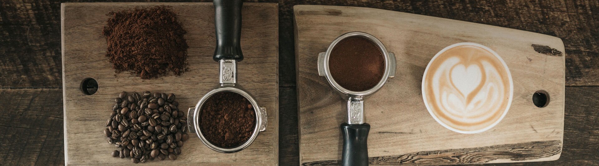 Frisch gemahlener Kaffee und Bohnen gepaart mit einer schön gestalteten Latte Art auf Holzbrettern.