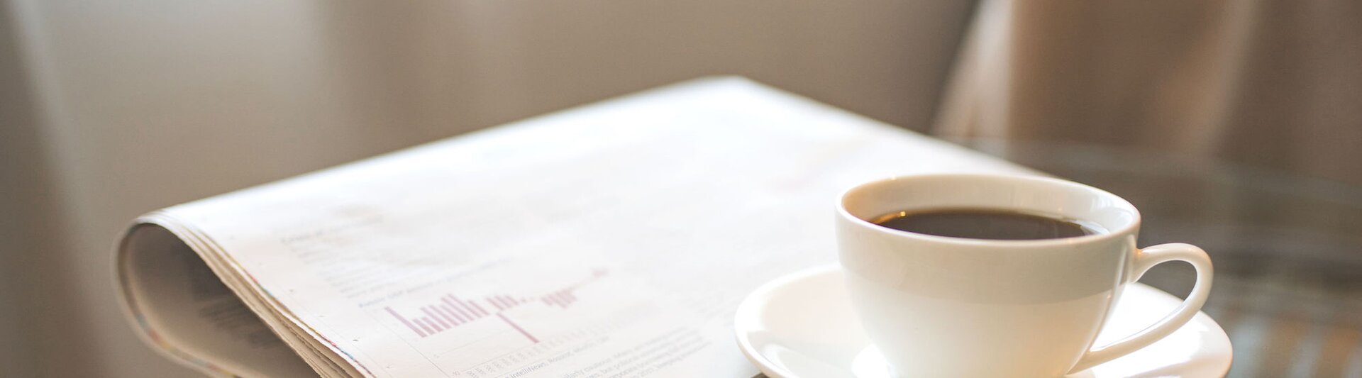 Frisch gebrühter Kaffee neben einer Zeitung, perfekt für einen Morgen voller Lektüre und aktueller beruflicher Neuigkeiten.