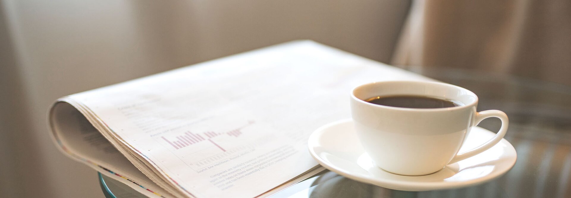 Frisch gebrühter Kaffee neben einer Zeitung, perfekt für einen Morgen voller Lektüre und aktueller beruflicher Neuigkeiten.