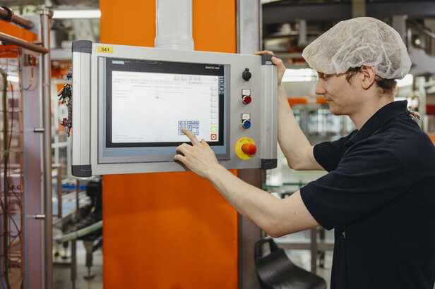 Bediener, der mit einem Siemens-Bedienpult in einer Produktionsanlage interagiert und einen effizienten Maschinenbetrieb sicherstellt.
