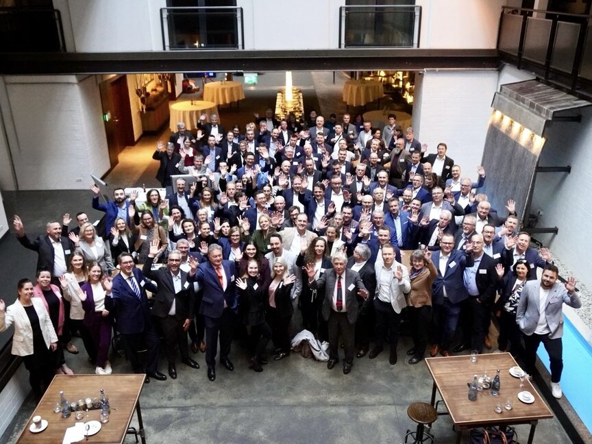 Networking-Veranstaltung mit verschiedenen Fachleuten, die winken und lächeln, in einem modernen Veranstaltungsort mit einer entspannten Atmosphäre.