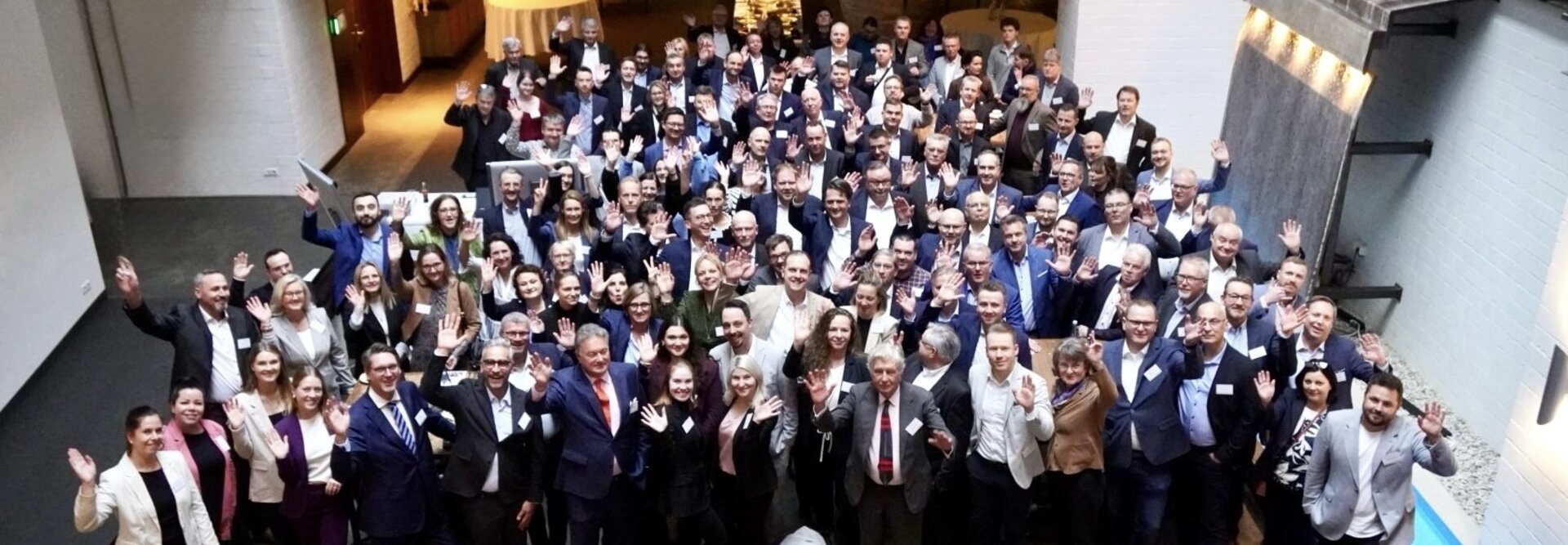 Networking-Veranstaltung mit verschiedenen Fachleuten, die winken und lächeln, in einem modernen Veranstaltungsort mit einer entspannten Atmosphäre.