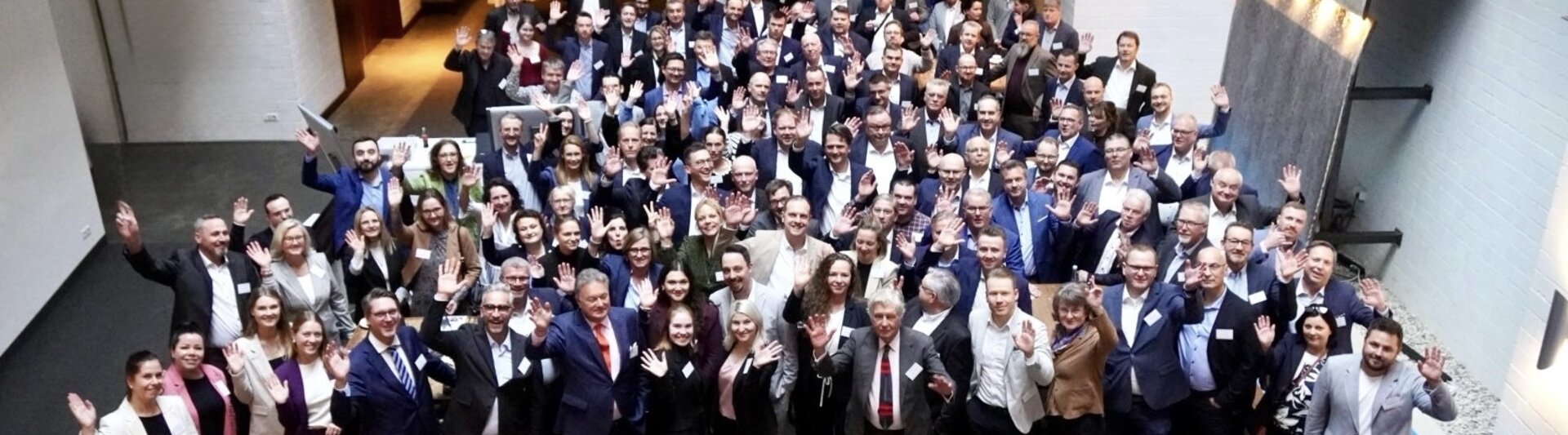 Networking-Veranstaltung mit verschiedenen Fachleuten, die winken und lächeln, in einem modernen Veranstaltungsort mit einer entspannten Atmosphäre.