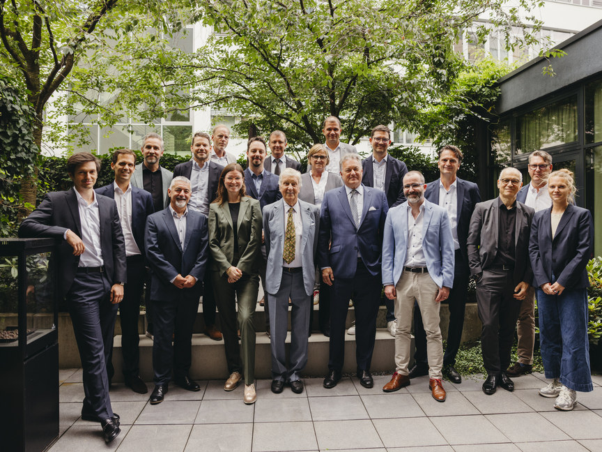 Führungskräfte aus der Wirtschaft versammeln sich für ein Gruppenfoto in einem üppigen städtischen Garten, um Zusammenarbeit und Professionalität zu demonstrieren.