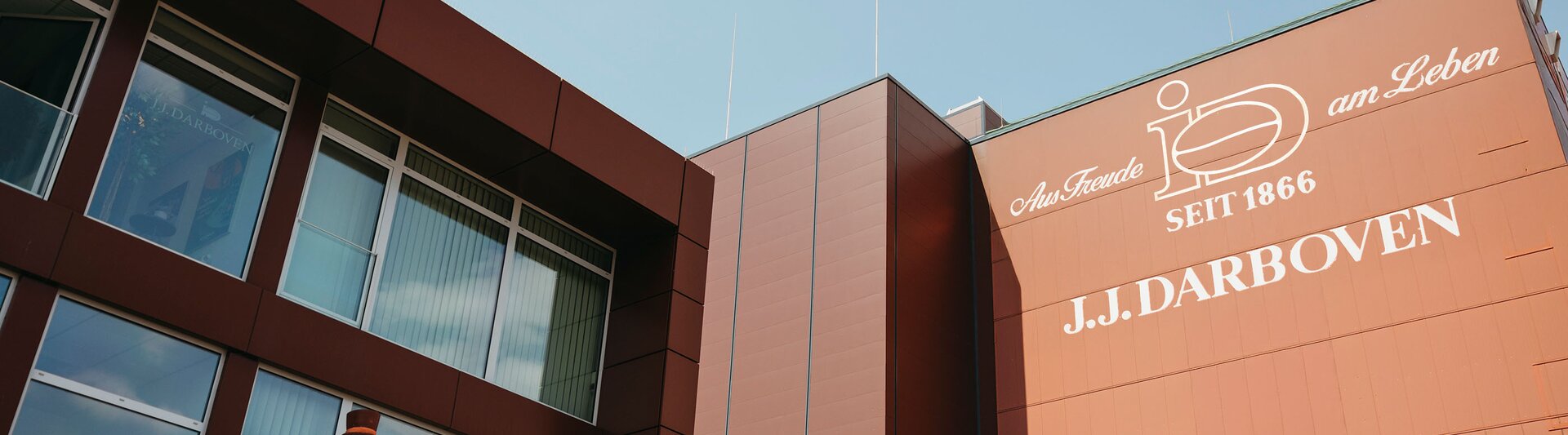 Fassade des J.J. Darboven-Gebäudes mit einer historischen Figur, die das Erbe des Unternehmens seit 1866 vor einem blauen Himmel zeigt.