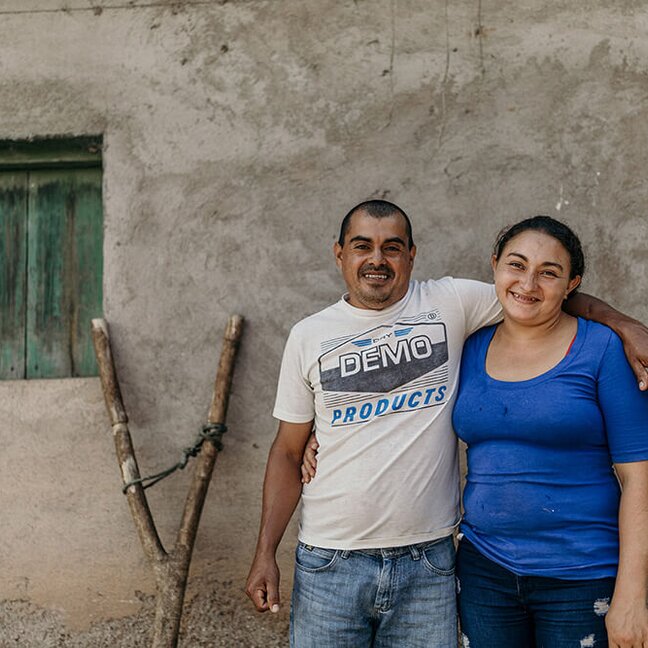 Smiling couple posing outdoors near their home, highlighting community and agricultural life.
