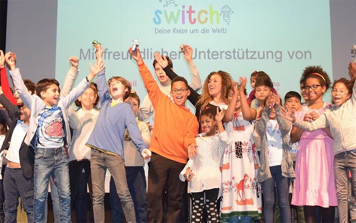 Freudig feiernde Kinder auf der Bühne der Switch-Veranstaltung, die das globale Bewusstsein und das Engagement in der Gemeinschaft fördert.